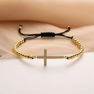 Detailed view of gold-plated cross bracelet with cubic zirconia on beige silk fabric