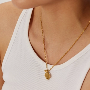Detailed close-up of a gold shell necklace with a white pearl on a ribbed tank top