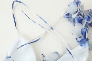 Détail d'une robe blanche fleurie avec fleurs 3D en tissu et fines bretelles croisées