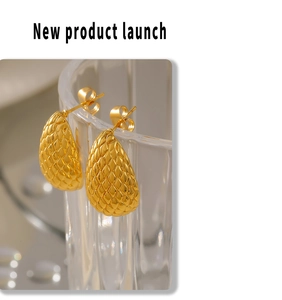 Macro shot of 18k gold plated teardrop earrings with textured scale design on glass