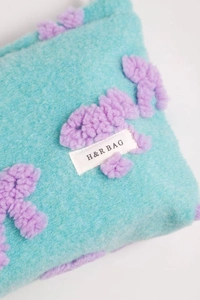 Detail of plush lamb wool makeup bag showing blue faux fur texture and purple floral decor