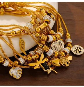 Detail of gold snake chains with tree of life, heart and dragonfly charms on wood