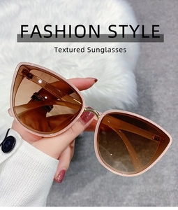 Detail of pink cat-eye sunglasses with tea gradient lenses held against white faux fur