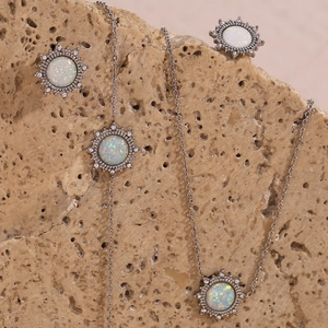 Detailed shot of silver sunburst necklace and earrings set with white opal on beige rock