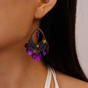 Close-up of bohemian bronze wire earrings with purple shell and floral bead details