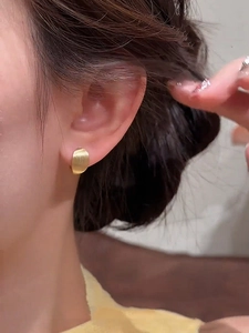 Close-up of 18k gold plated brushed oval hoop earring worn on a female ear