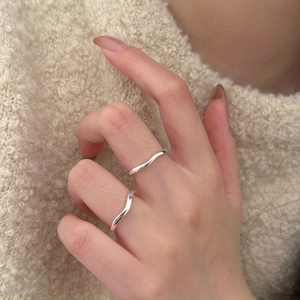 Close-up of minimalist sterling silver wavy rings worn by model on textured fabric