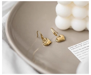 Close-up of golden vintage heart earrings on a ceramic tray with aesthetic decor