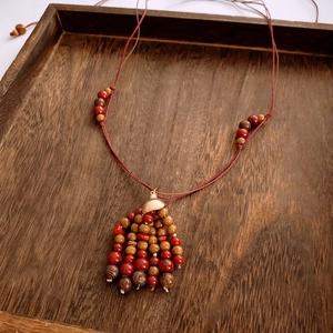 Detailed close-up of ethnic beaded necklace with red tassels on a rustic wood tray
