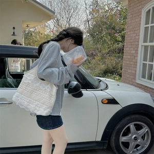 Sac à bandoulière en dentelle avec volants porté par un mannequin près d'une voiture