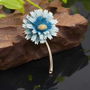 Detail of blue and white enamel flower brooch with golden stem on dark wood base