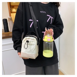 Detail view of a canvas drawstring crossbody bag with an adjustable strap and a water bottle