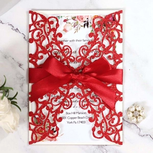 Red glitter laser-cut wedding invitation with satin bow and floral insert on marble
