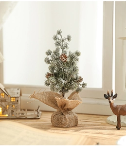 Close-up of mini snow-flocked Christmas tree with pine cones and rustic burlap base