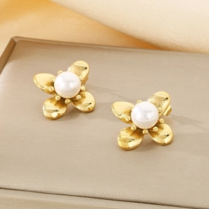 Macro detail of gold flower earrings with central white pearl on beige fabric