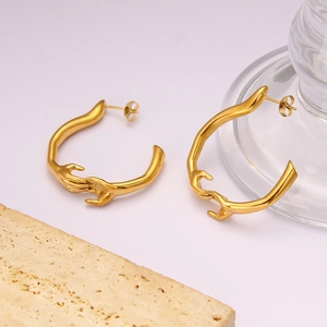 Détails macro des boucles d'oreilles mains entrelacées en acier doré sur marbre