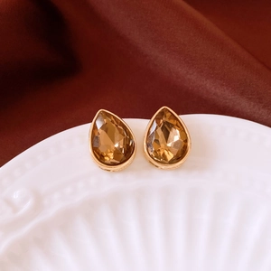 Detail view of water-drop champagne gold earrings on textured porcelain and silk background