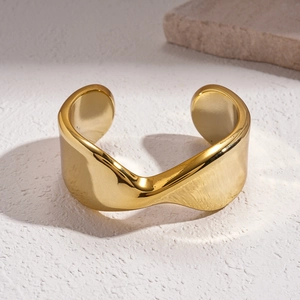 Close-up of golden wide wave cuff bracelet with polished finish on white textured stone