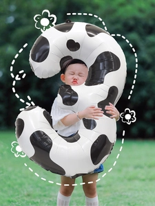 Large number 3 balloon with cow print pattern held by a toddler in an outdoor party setting