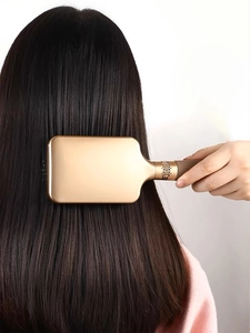 Detail of champagne gold paddle hair brush gliding through long straight dark hair