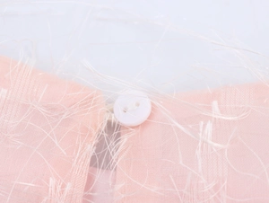 Dettaglio del vestito rosa con piume, bottone bianco e texture con frange decorative