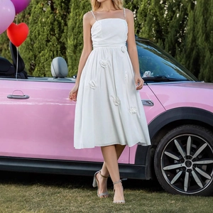 Detail of white midi dress featuring 3D floral accents and sleek spaghetti straps