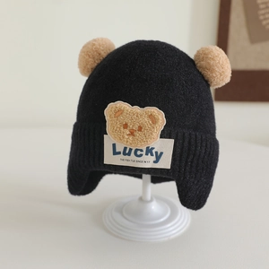 Close-up of black knit baby winter hat with double pom poms and cute teddy bear patch