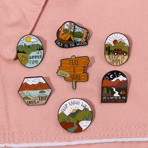 Outdoor camping themed enamel pins with mountains and tents on pink denim background