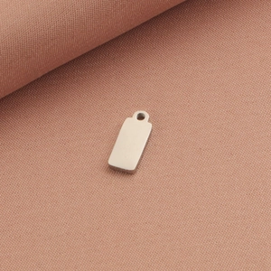 Close-up of a blank rectangular stainless steel tag with small hole on pink fabric