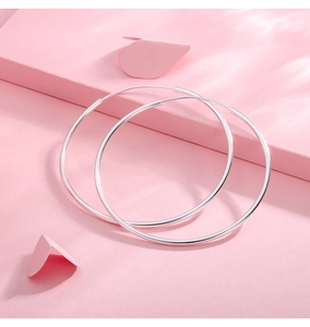 Macro shot of minimalist S999 sterling silver hoop earrings on a soft pink background