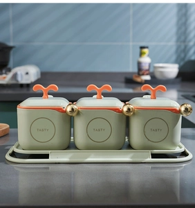 Close-up of three grey-green seasoning jars with orange handles and gold lids on a tray