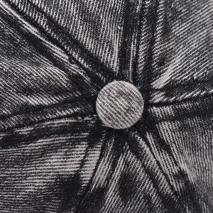 Macro view of the top button and radial stitching on this distressed denim baseball cap