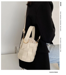 Detail of cream woven bucket bag with gold rings shown on model for crossbody wear