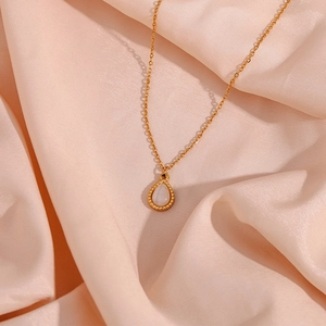 Macro shot of gold teardrop pendant necklace with cat eye stone on pink silk background