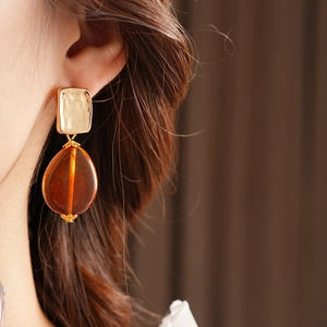 Close-up of model wearing amber teardrop earrings with a golden square stud and cap