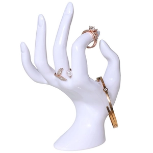 Close-up of a white plastic hand-shaped display stand holding rose gold rings and jewelry