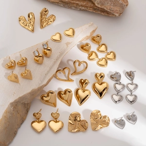 Minimalist gold heart earrings collection displayed on a natural light stone background