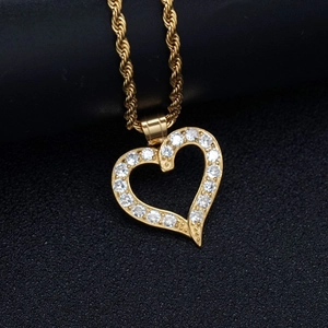 Golden heart pendant necklace with clear crystals on a textured black background
