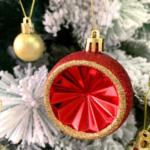 Close-up of red and gold glitter Christmas ornaments hanging on a snowy tree branch
