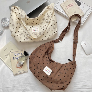 Flat lay of corduroy crescent crossbody bags with heart and bow patterns on white fabric