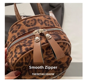 Close-up of smooth silver dual zippers and brown leather pulls on a leopard print mini backpack