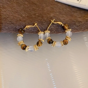 Détail de créoles dorées avec perles œil de tigre ambrées et pierres semi-transparentes