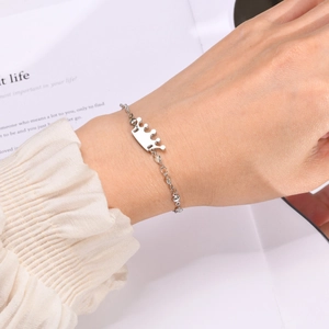 Detail of silver crown pendant bracelet on wrist with elegant ruffled sleeve background
