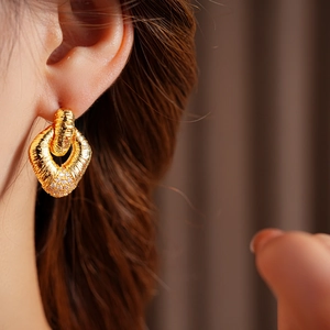 Close-up of golden woven texture earrings with white pavé crystals on model
