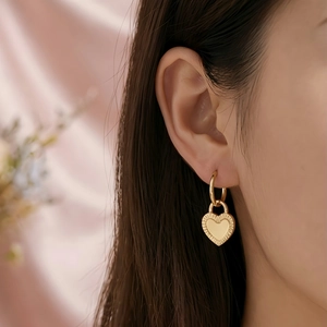 Close-up of golden heart earrings with textured design worn by a model on pink fabric