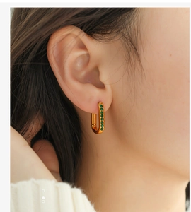 Close-up of gold-plated rectangular hoop earrings with emerald green gemstones on ear