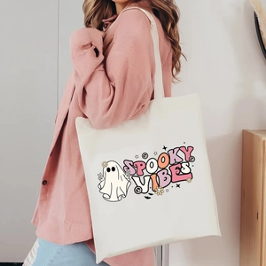 Detail of white canvas tote bag featuring spooky vibes ghost print worn with pink shirt