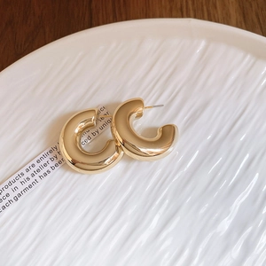 Detailed close-up of golden C-shaped hoop earrings on a white textured ceramic dish