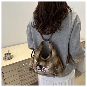 Detailed view of brown plaid backpack with cute dog illustration worn by a person