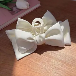Détail de la pince à cheveux à double nœud en satin blanc sur une table en bois